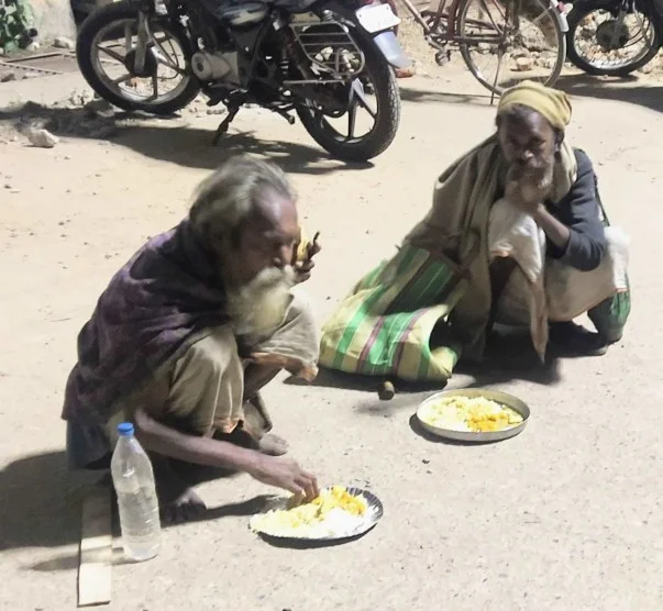 Two elderly men eating prepared meals outdoors